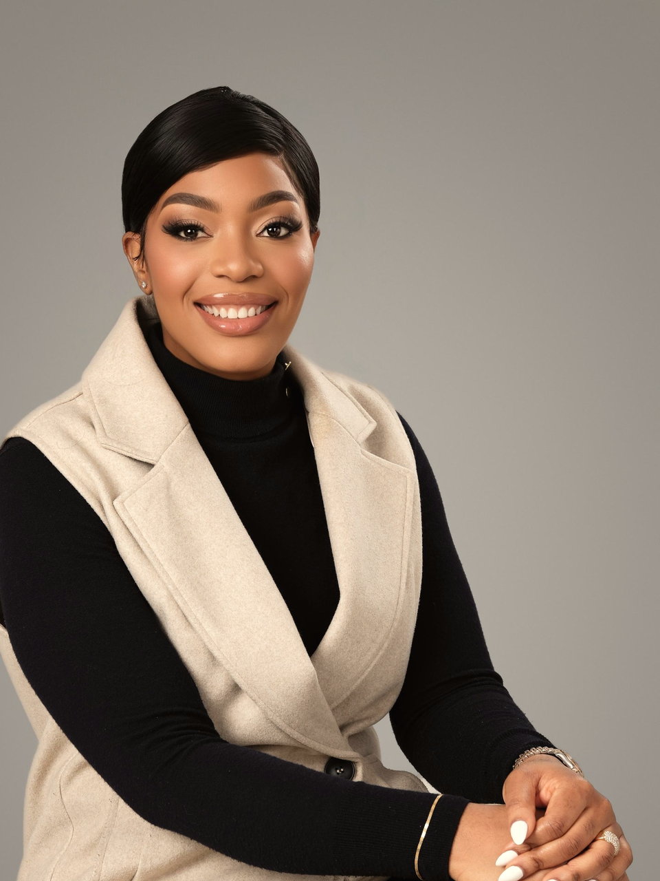Nnedi Okafor, seated and smiling, wearing a cream tailored waistcoat over a black roll-neck.
